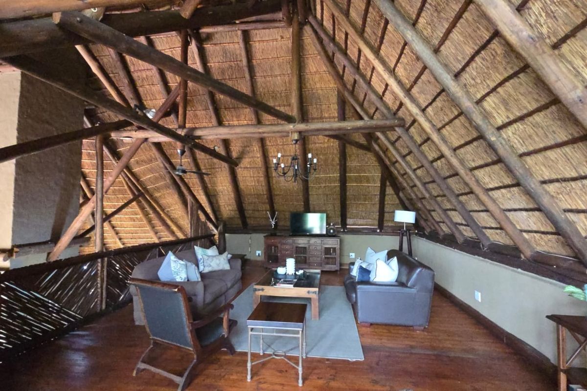 Spacious loft-style living area featuring a high vaulted thatched roof with exposed timber trusses and warm wooden flooring.