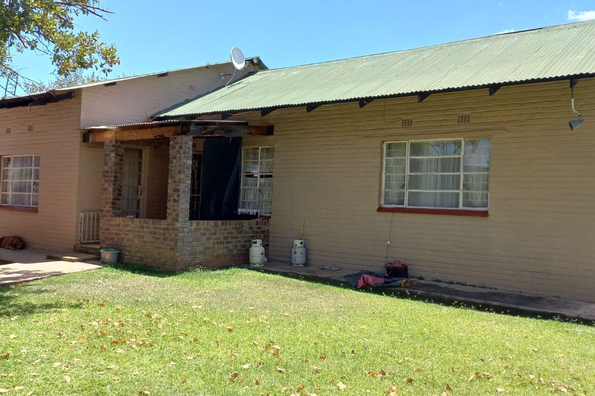 Rear view of a farm-style dwelling featuring a corrugated metal roof, brick porch structure, and large windows overlooking a grassy garden area.