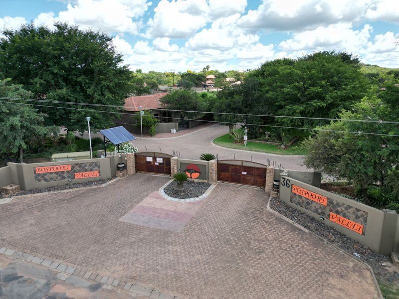 Aerial view of the secure entrance to Bospoort Vallei, featuring a paved driveway, gated access, boundary walls, and solar-powered infrastructure.