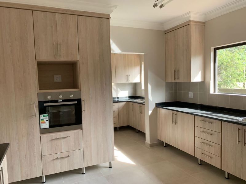 Modern kitchen featuring light wood-grain cabinetry, dark stone countertops, tiled backsplash, and a built-in oven, with an adjoining scullery area.