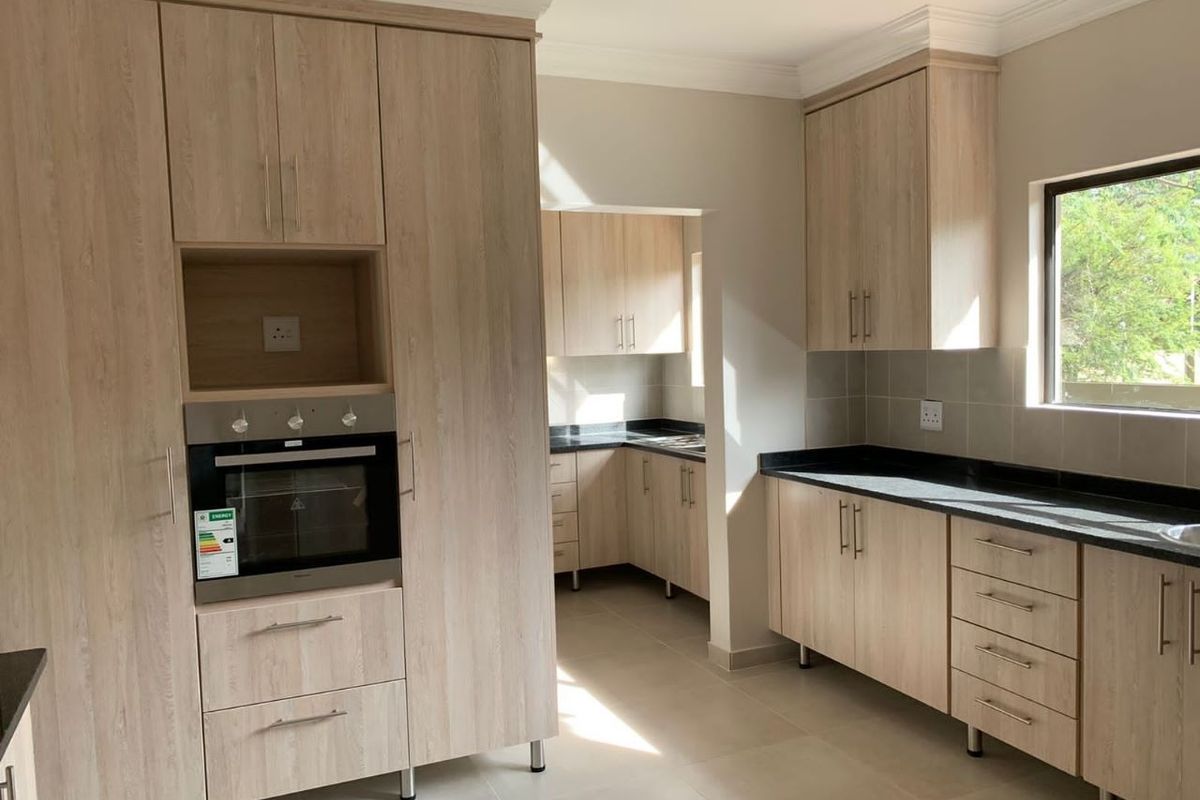 Modern kitchen featuring light wood-grain cabinetry, dark stone countertops, tiled backsplash, and a built-in oven, with an adjoining scullery area.