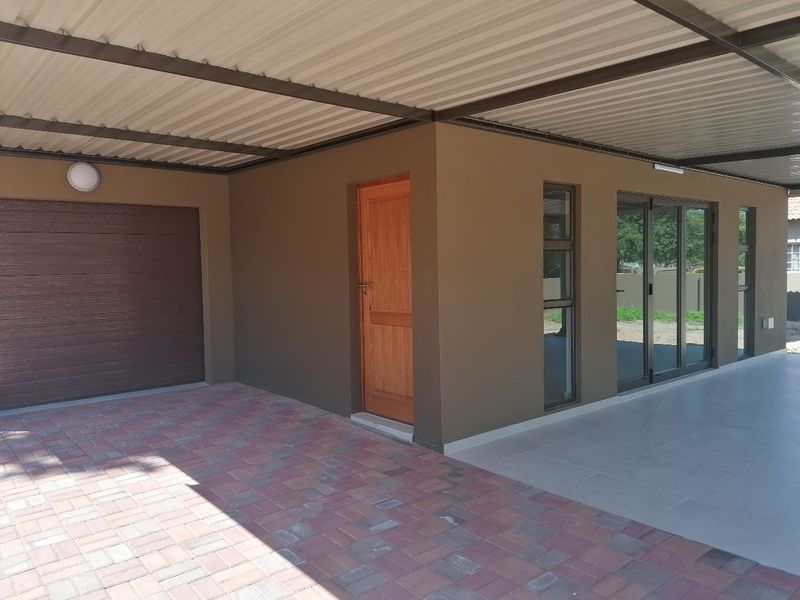 A well-maintained townhouse exterior featuring a paved driveway, covered parking area, modern garage door, and tiled patio entrance with aluminium framed windows.