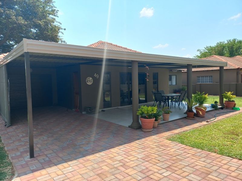Front view of the townhouse featuring a spacious covered patio, paved driveway, and well-maintained exterior finishes with sliding glass door access.