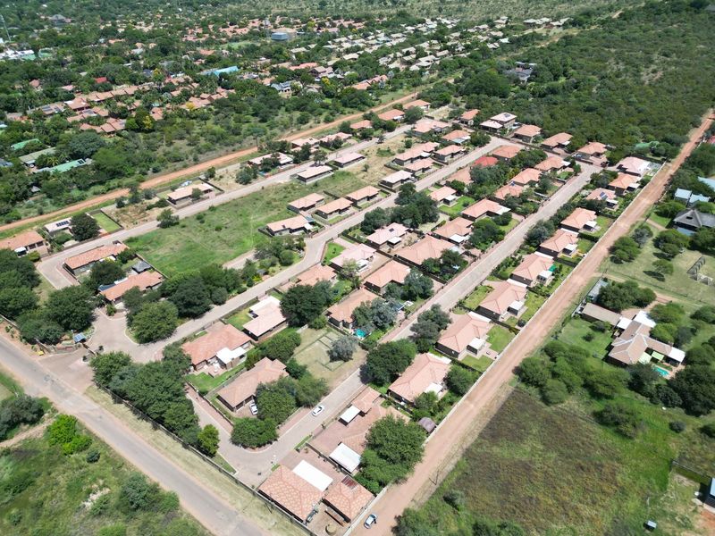 An aerial view of a residential townhouse estate featuring multiple detached units with tiled roofs, paved access roads, and established garden areas.