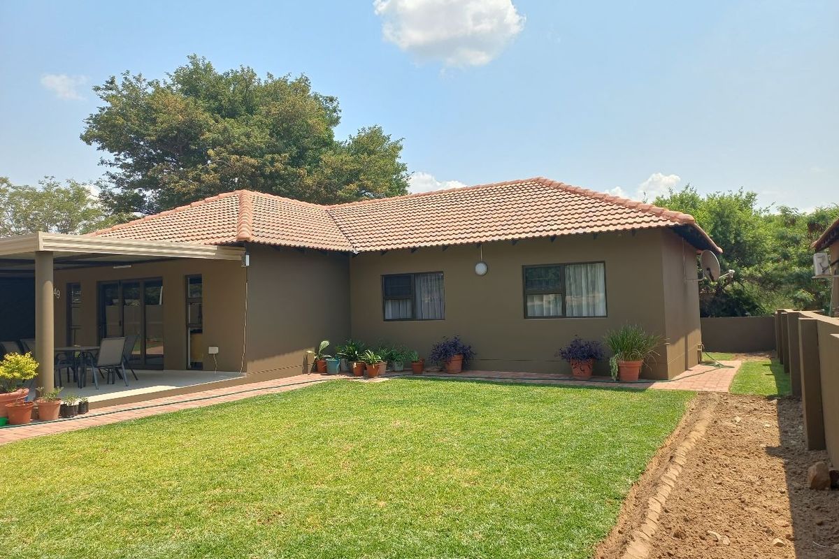 Rear view of the townhouse featuring a covered patio, paved walkway, and a well-maintained lawn area.