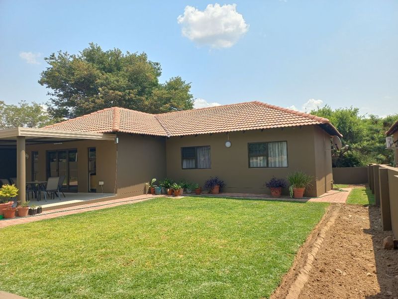 Rear view of the townhouse featuring a covered patio, paved walkway, and a well-maintained lawn area.