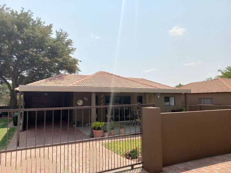 Front view of a townhouse featuring a tiled roof, paved driveway, secure metal gate, and a covered patio entrance.