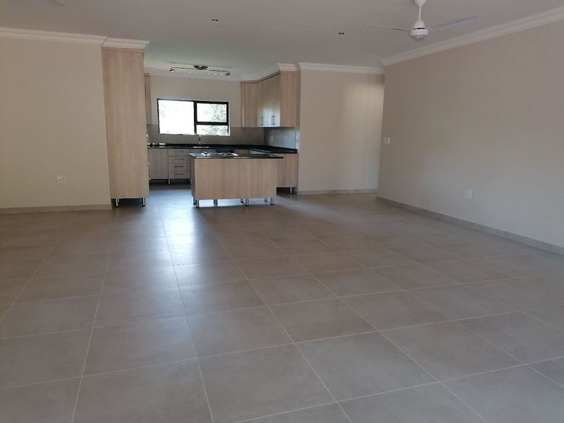 Spacious open-plan living area featuring large format floor tiles, neutral walls, and a modern kitchen with built-in cabinetry and a central island.