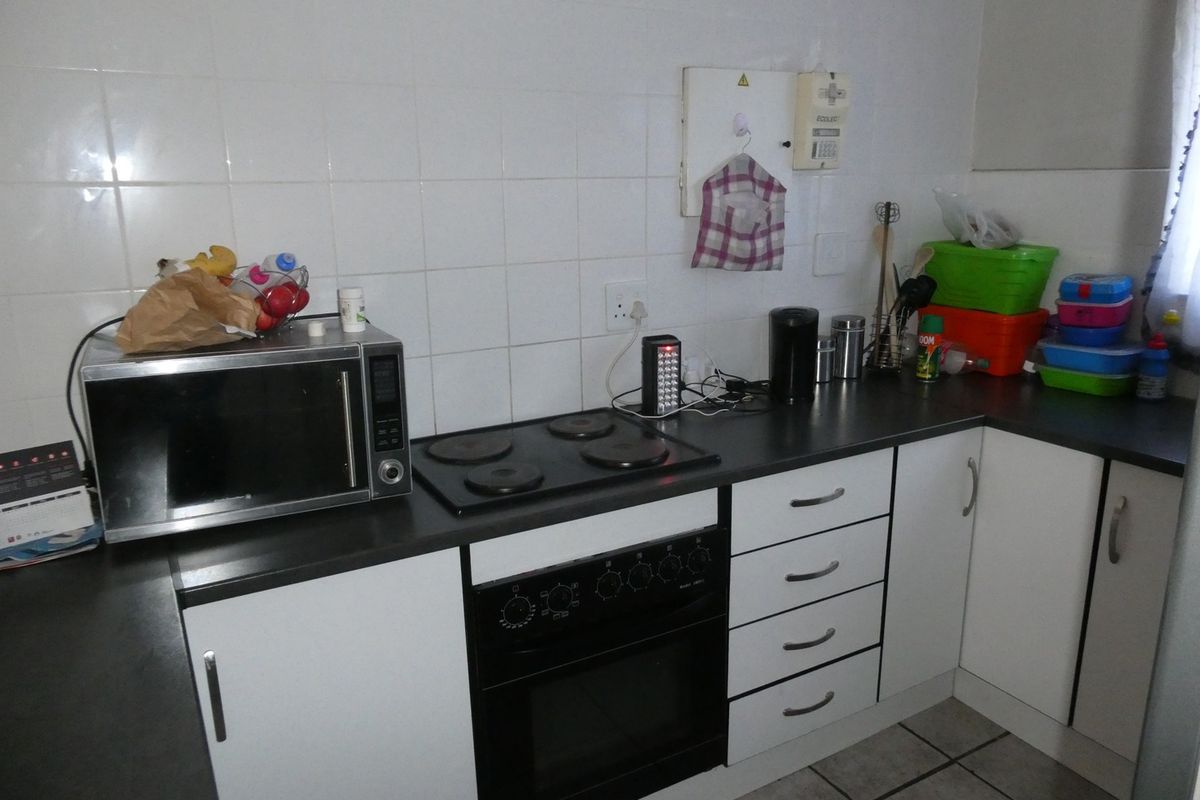 Compact kitchen featuring white cabinetry, dark laminate countertops, a built-in electric oven with hob, and tiled splashback.