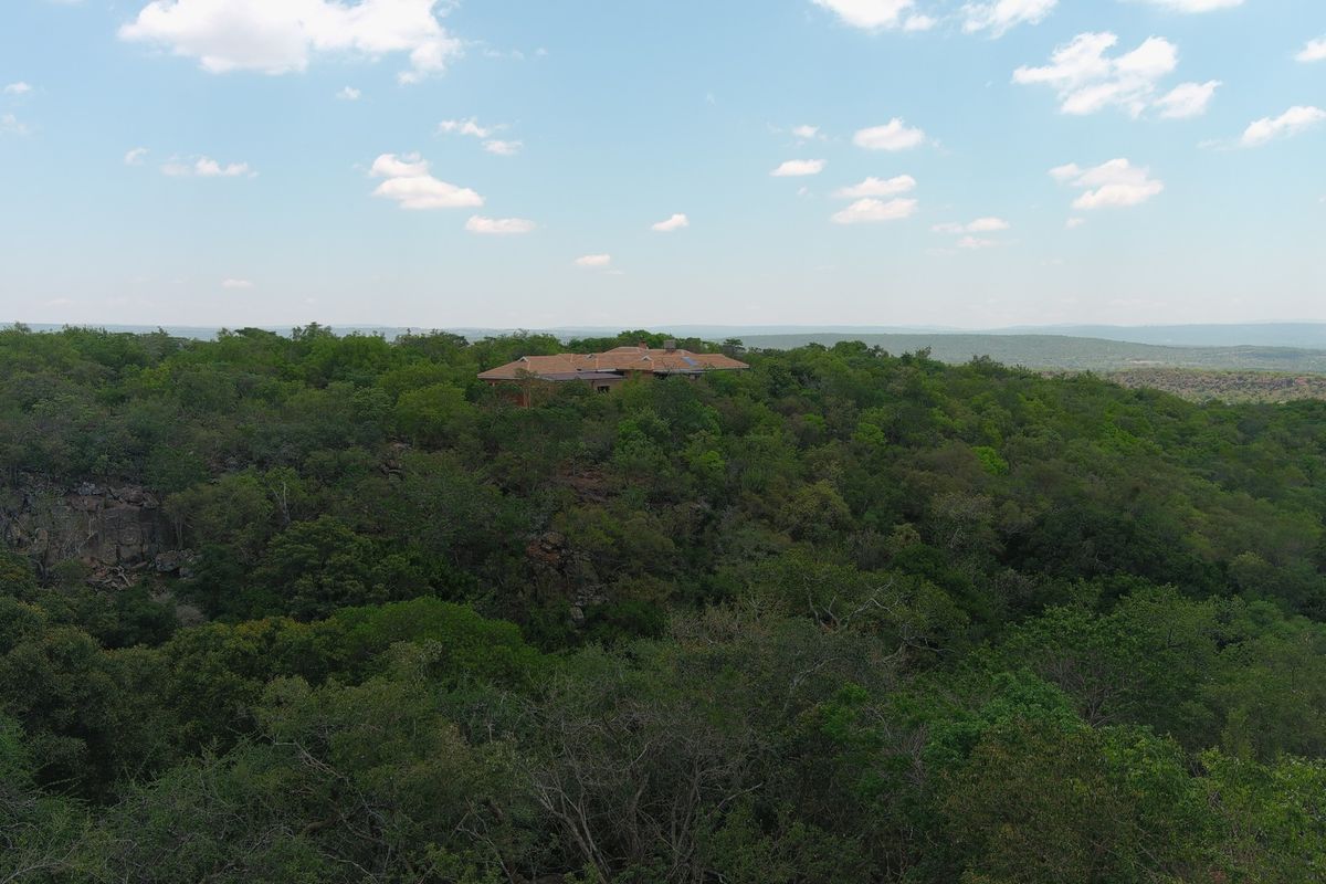 An aerial view of a residential property nestled within a dense, natural woodland landscape.