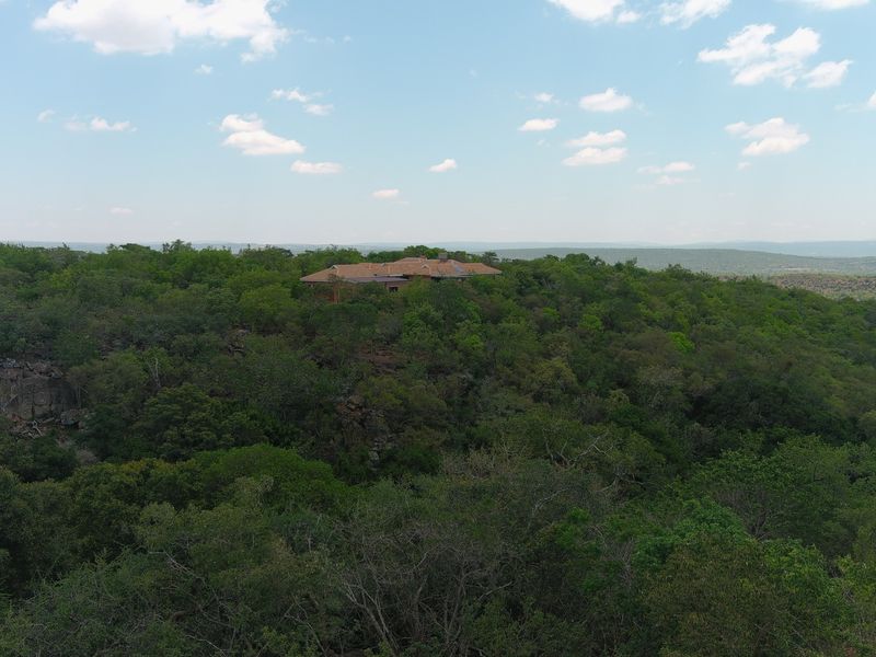 An aerial view of a residential property nestled within a dense, natural woodland landscape.