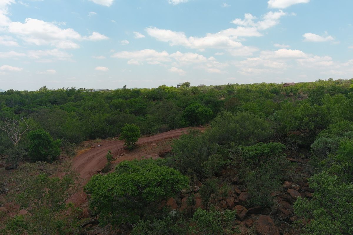 An aerial view of a vacant residential plot featuring natural bushveld vegetation, rocky terrain, and an unpaved access road.