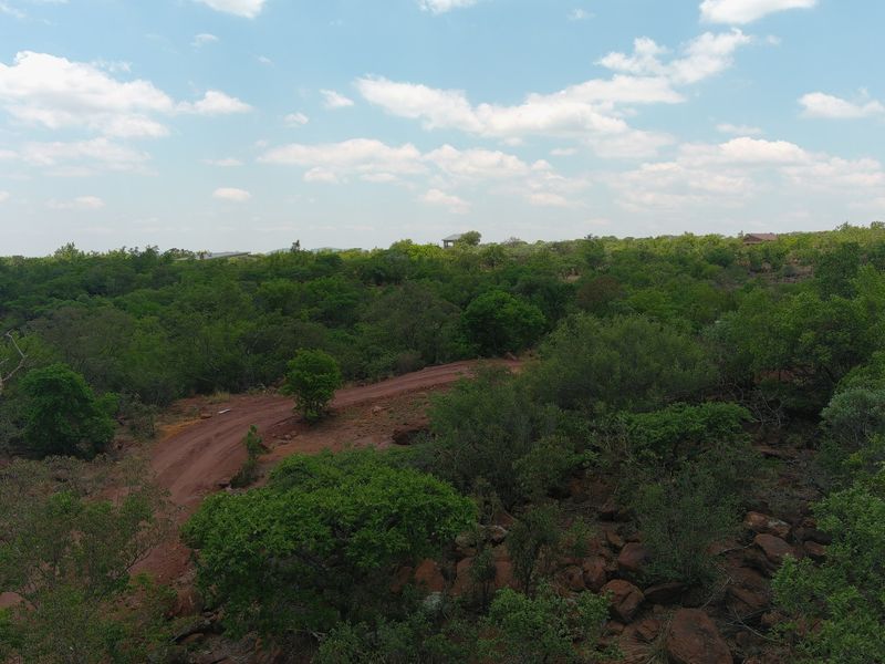 An aerial view of a vacant residential plot featuring natural bushveld vegetation, rocky terrain, and an unpaved access road.