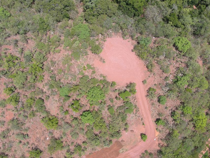 Aerial view of a vacant residential plot featuring a cleared building site and a dirt access road surrounded by natural vegetation.