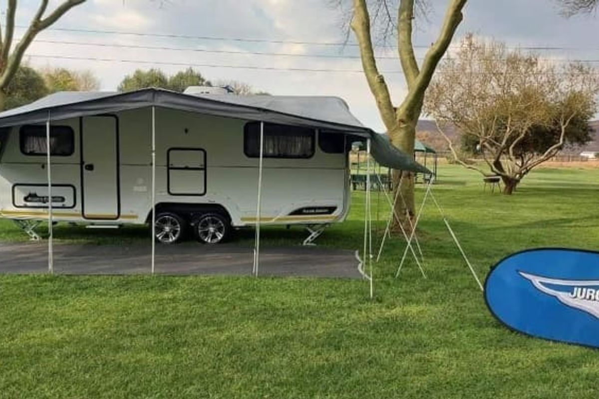 A caravan parked on a grassy lodge site with an extended canopy, set within a spacious outdoor recreational area.