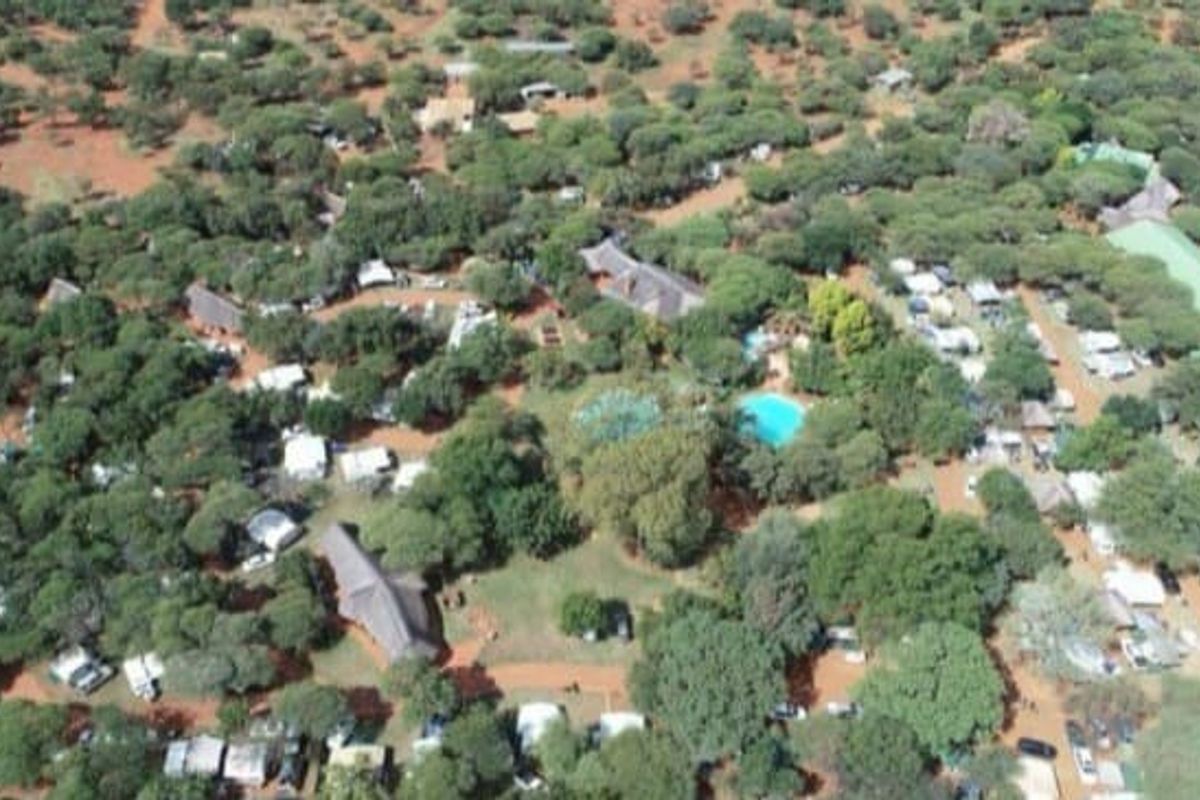 An aerial view of a lodge property featuring multiple thatched roof buildings, a swimming pool, and extensive natural vegetation.