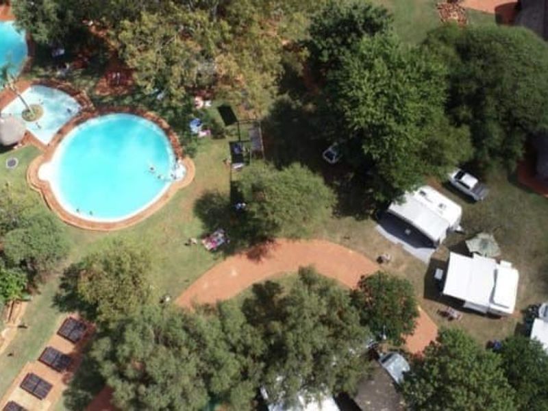 Aerial view of the lodge grounds featuring multiple swimming pools, mature trees, landscaped garden areas, and established pathways throughout the property.