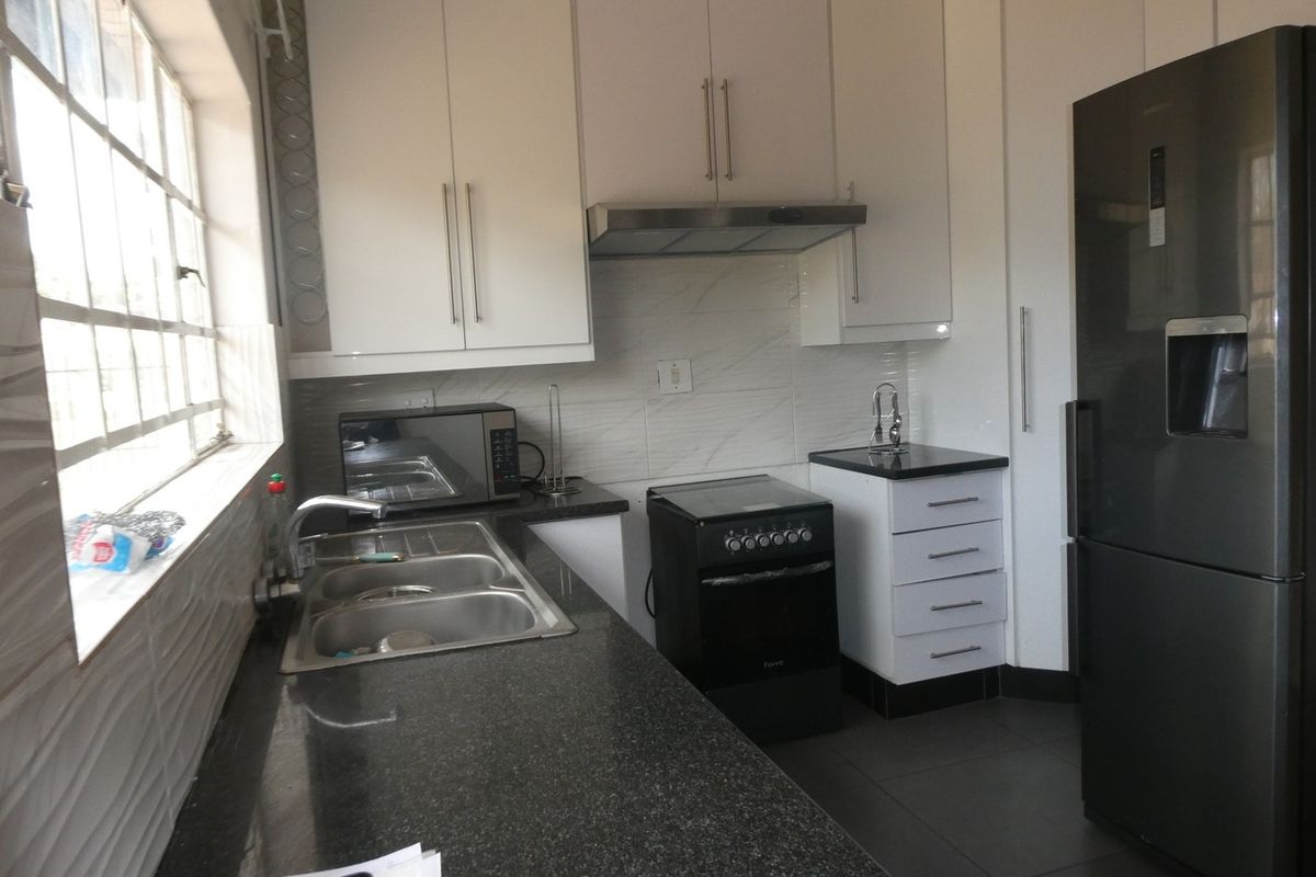 A functional kitchen featuring white cabinetry, dark granite countertops, a double sink, and a built-in extractor fan with tiled splashbacks.