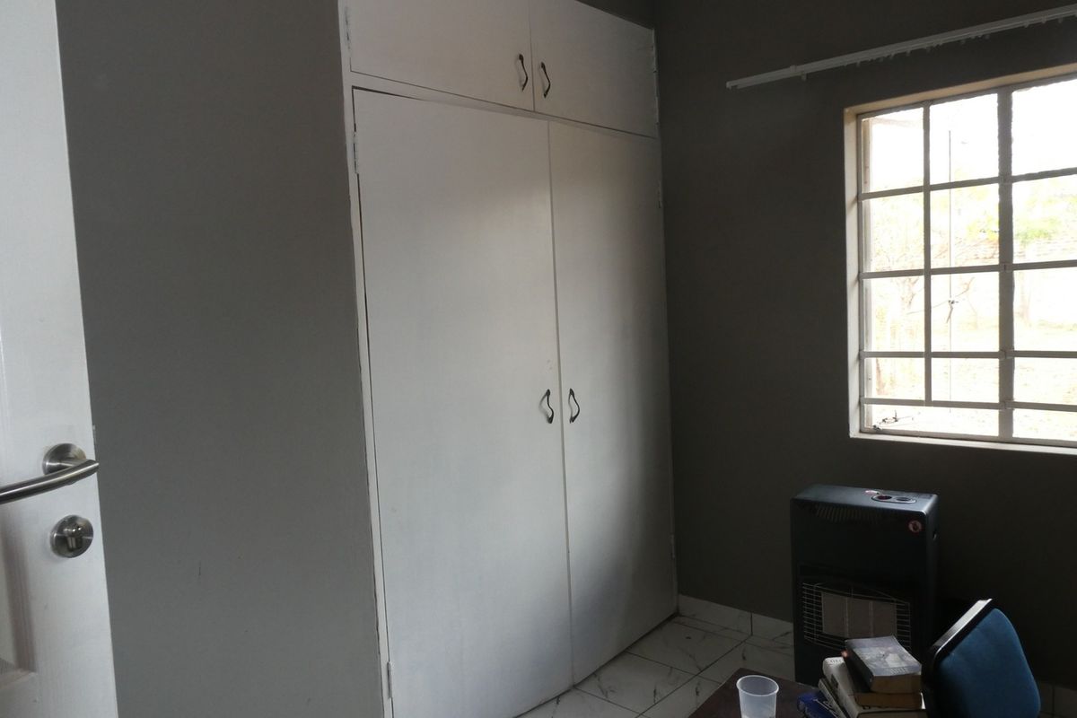 A bedroom featuring built-in cupboards, tiled flooring, and a window with security bars, providing a functional and neutral living space.