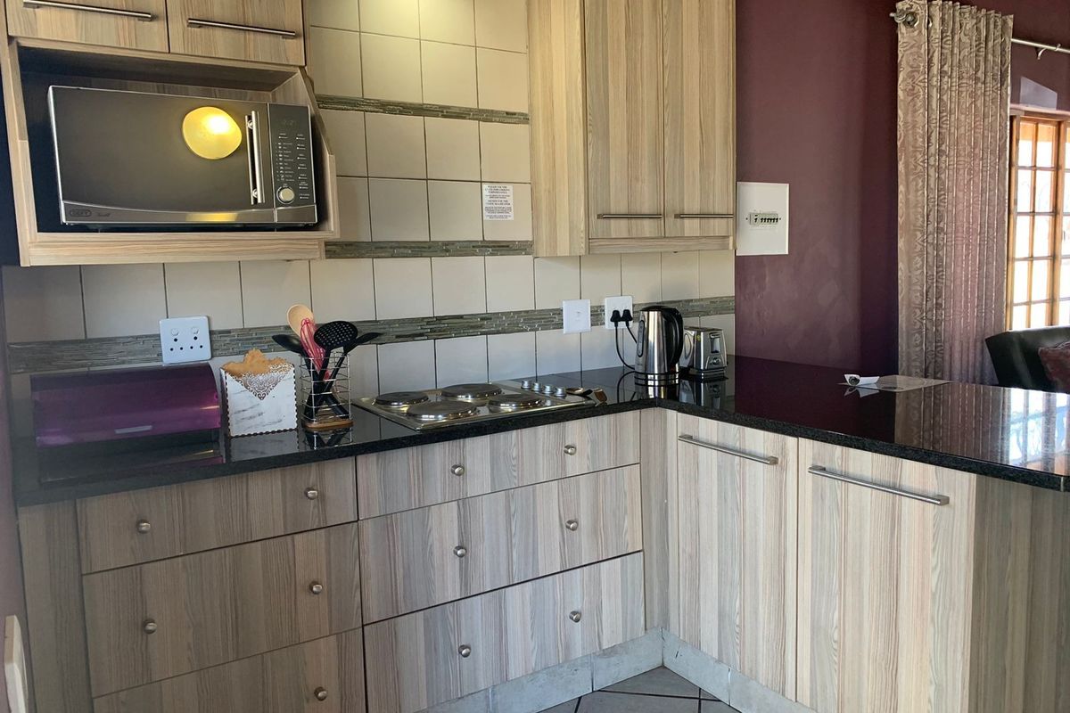 A functional kitchen featuring light wood-grain cabinetry, dark granite countertops, a built-in hob, and a microwave, complemented by a tiled backsplash and floor.