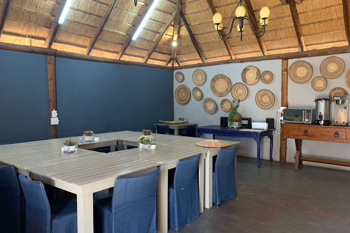 A spacious lodge-style living area featuring a high thatched roof with exposed timber rafters, decorative wall baskets, and integrated lighting.