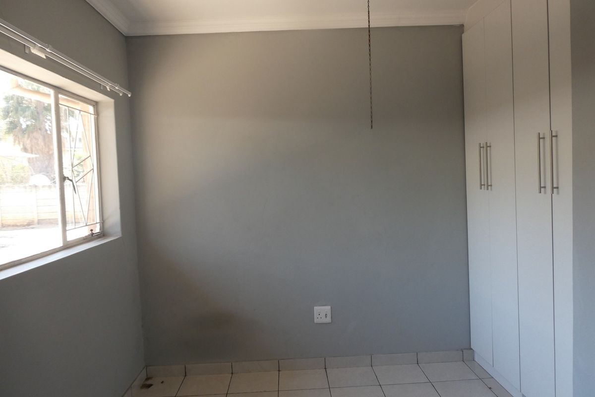 A bedroom featuring neutral grey walls, tiled flooring, and built-in white cabinetry with modern handles.