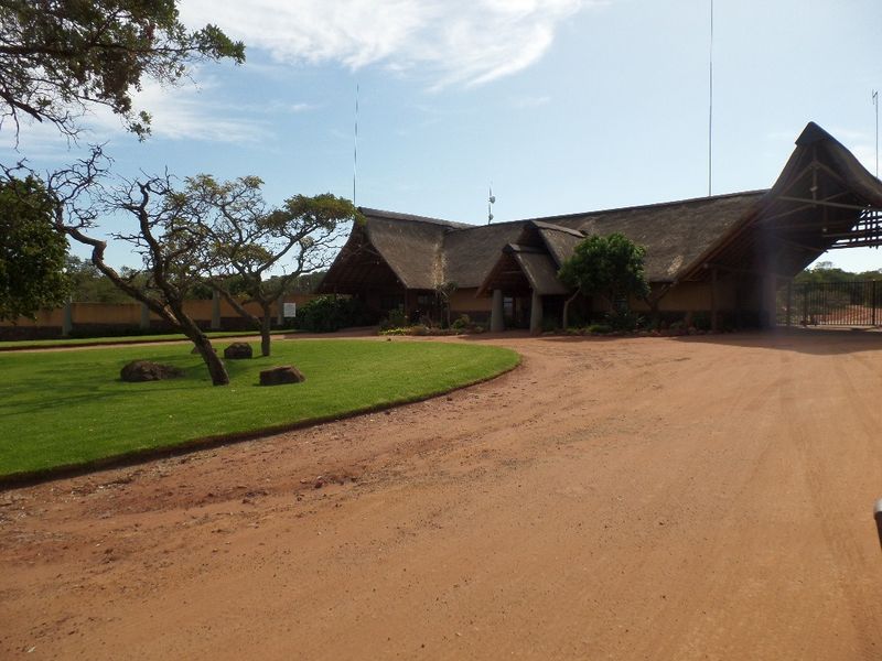 Front elevation of a property featuring a traditional thatch roof, expansive driveway, and well-maintained lawn area.