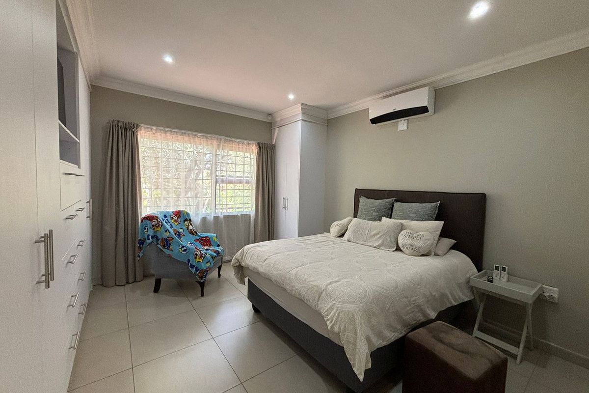 A well-maintained bedroom featuring built-in cupboards, tiled flooring, recessed ceiling lighting, and a wall-mounted air conditioning unit.