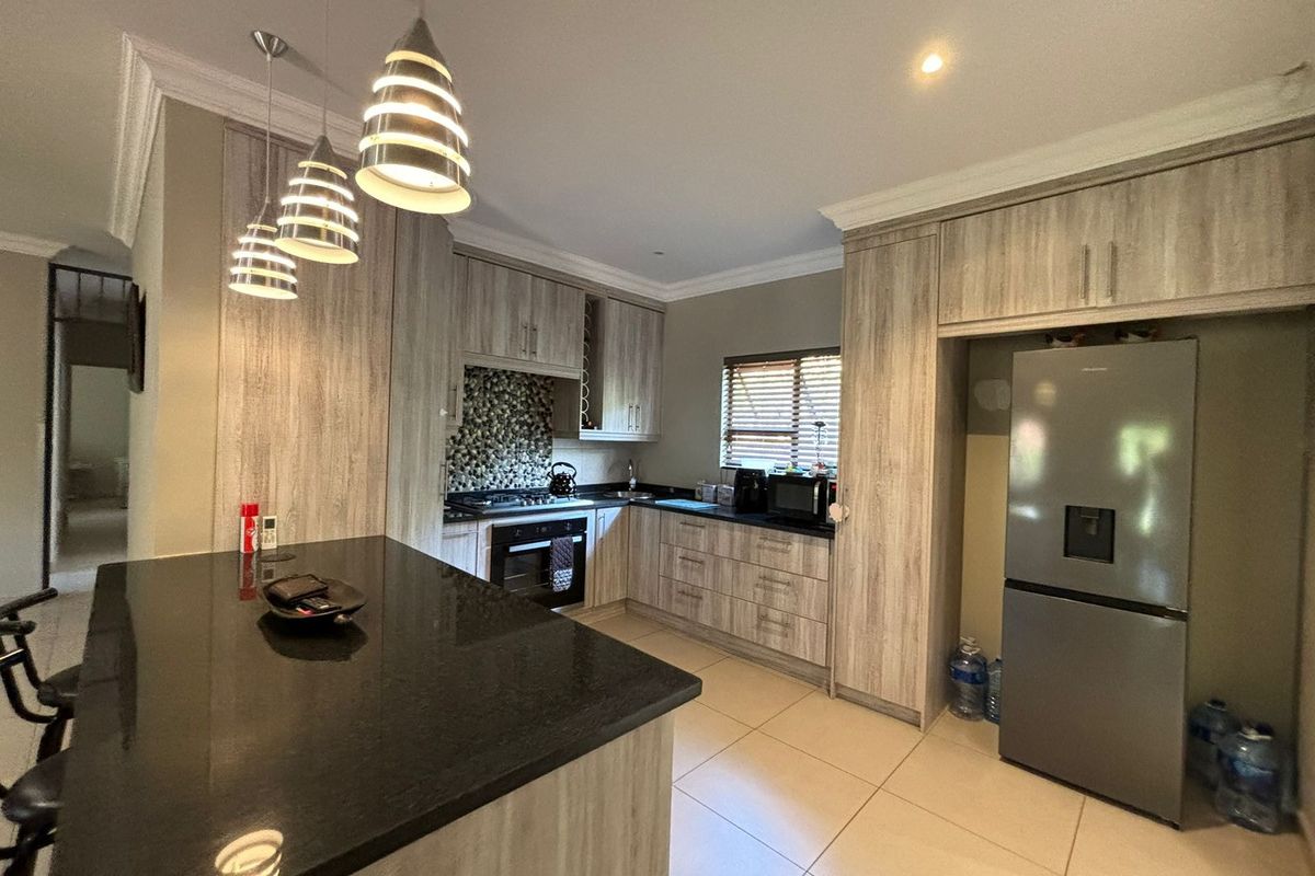 Modern kitchen featuring light wood-grain cabinetry, a large black granite island, built-in oven, gas hob, and tiled flooring.