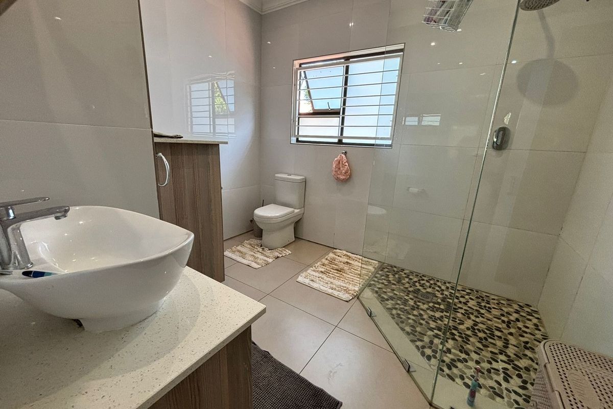 Modern bathroom featuring a glass-enclosed shower with pebble-style flooring, a contemporary vanity with a vessel sink, and a standard toilet.