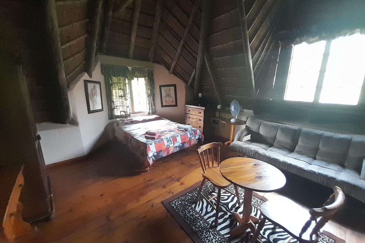 A rustic bedroom featuring a high thatched roof with exposed timber beams, timber flooring, and natural light from multiple windows.