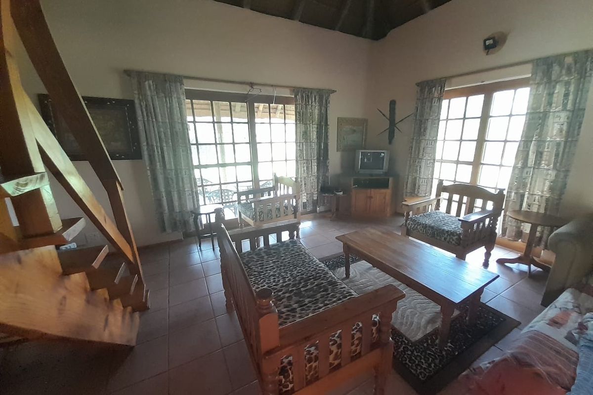 A rustic living room featuring a high thatched ceiling, tiled flooring, and double glass doors providing natural light and access to the exterior.