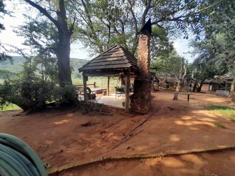 Outdoor covered patio area featuring a rustic stone fireplace and thatched roof, set within a natural farm landscape.
