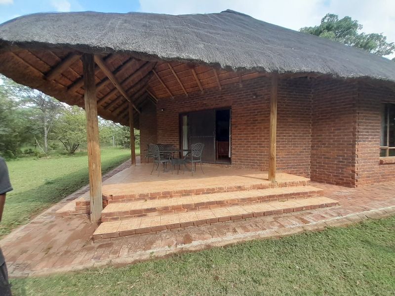 A rustic covered patio featuring a traditional thatched roof, exposed timber beams, and brick construction, overlooking the surrounding farm landscape.