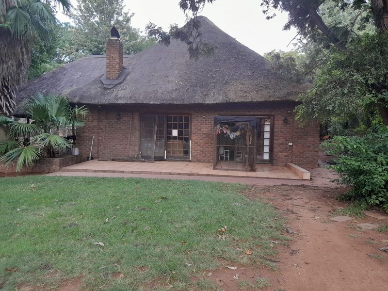 Rear view of a traditional thatched-roof farmhouse featuring an exposed brick facade and a tiled patio area set within a mature garden.
