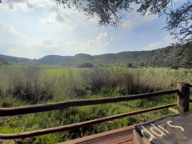Scenic landscape view overlooking natural grasslands and hills, framed by a rustic timber railing on a wooden deck.