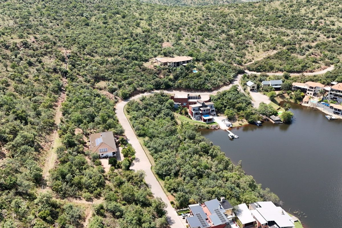An aerial view of a residential estate featuring paved roads, native bushveld vegetation, and direct waterfront access to a dam or lake.
