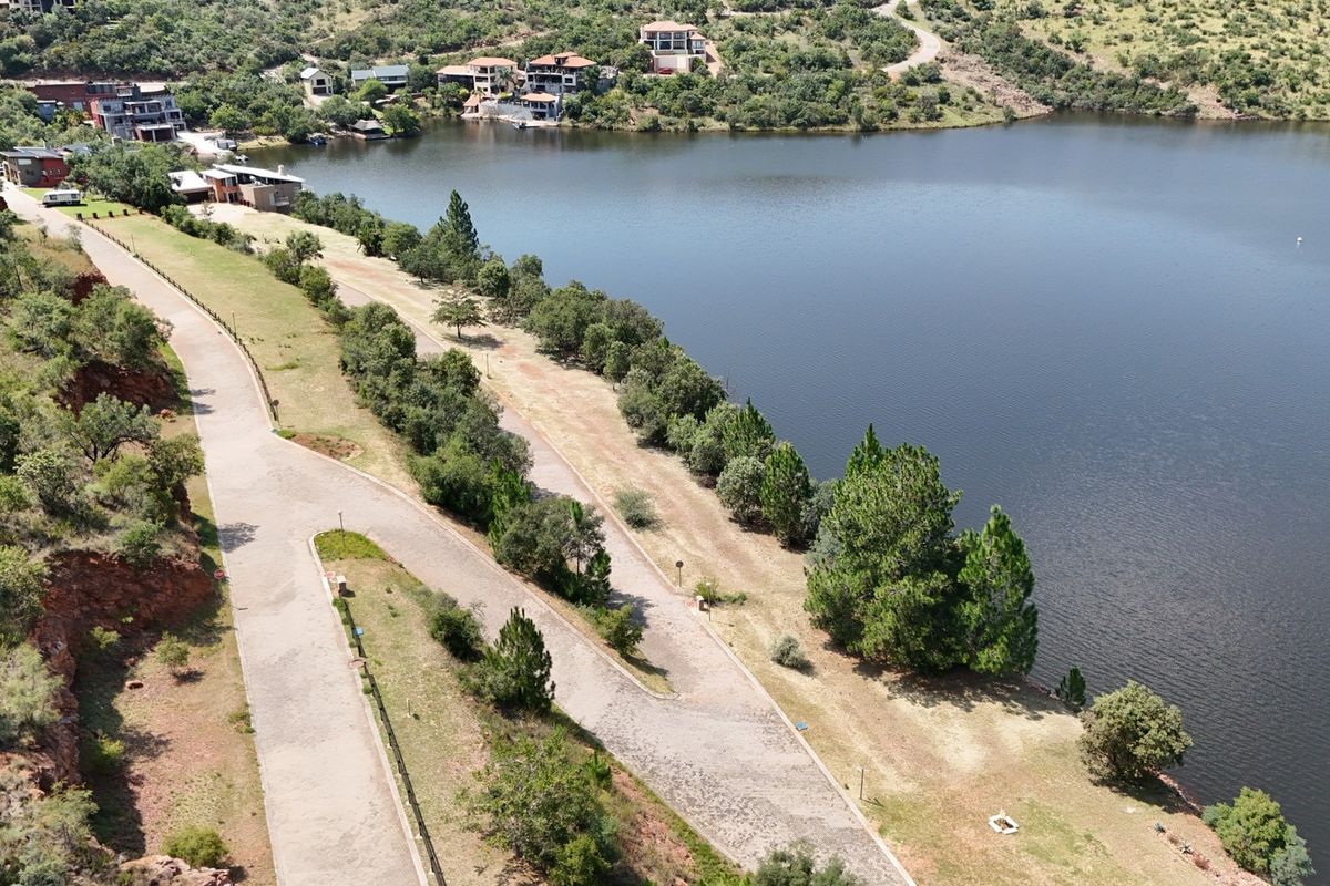 Aerial view of a vacant residential plot featuring paved road access and direct frontage onto a large lake within a scenic estate setting.