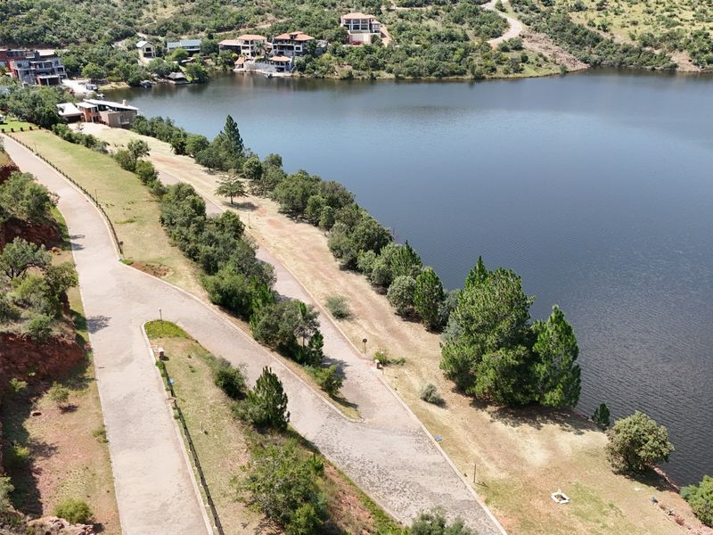 Aerial view of a vacant residential plot featuring paved road access and direct frontage onto a large lake within a scenic estate setting.