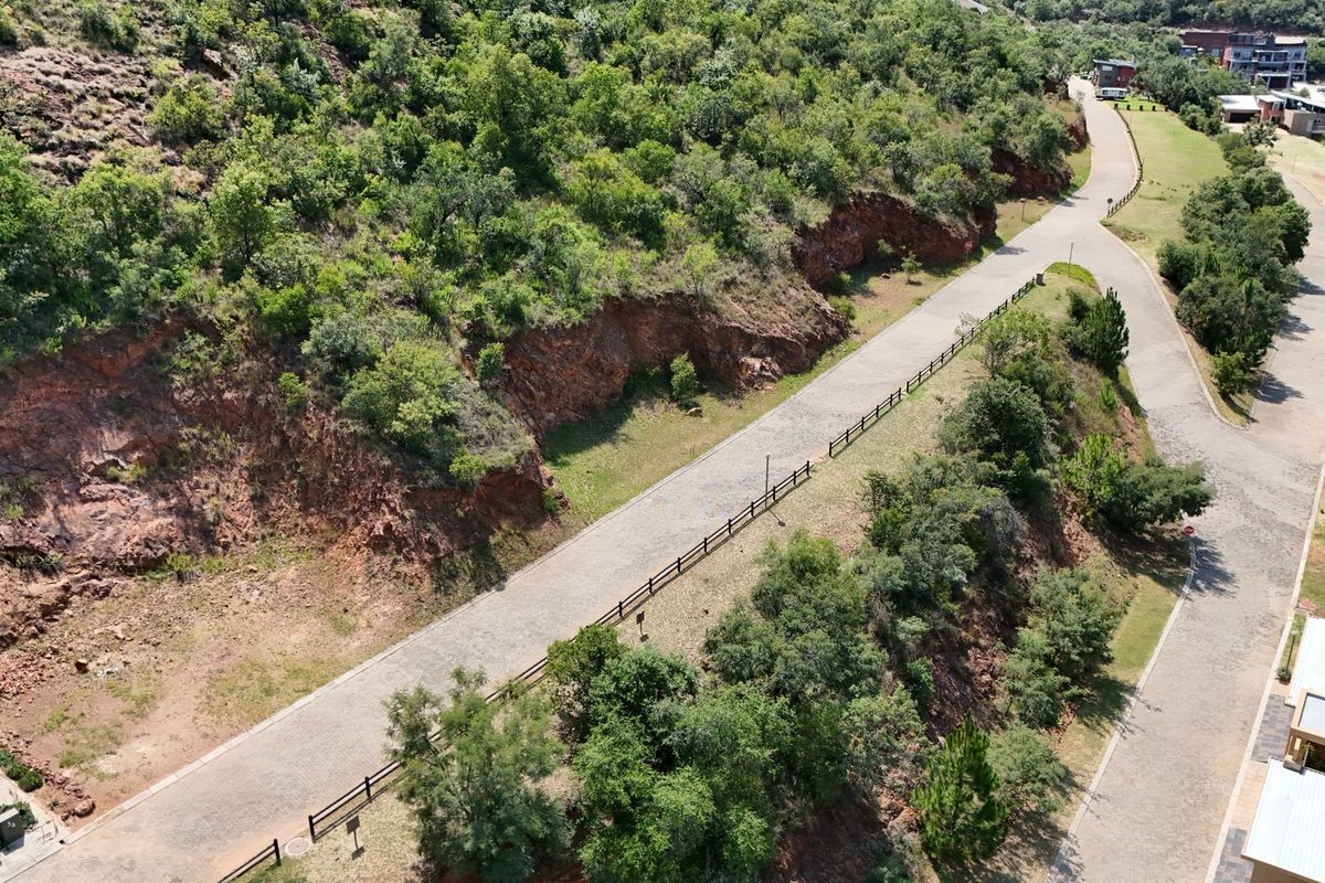 Aerial view of a residential estate featuring a paved road, post and rail fencing, and natural rocky terrain with established vegetation.