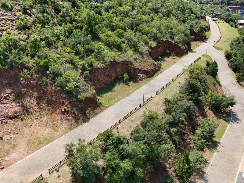 Aerial view of a residential estate featuring a paved road, post and rail fencing, and natural rocky terrain with established vegetation.