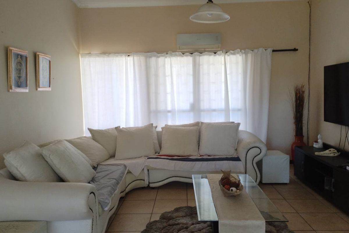 A comfortable living room featuring tiled flooring, a wall-mounted air conditioning unit, and large windows with natural light.