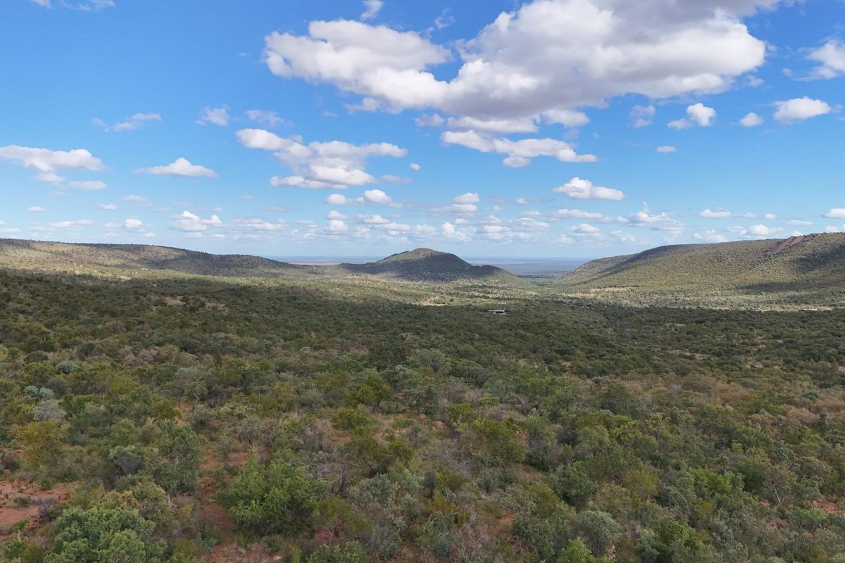 An expansive aerial view of the natural landscape, showcasing rolling hills and native vegetation under a clear blue sky.