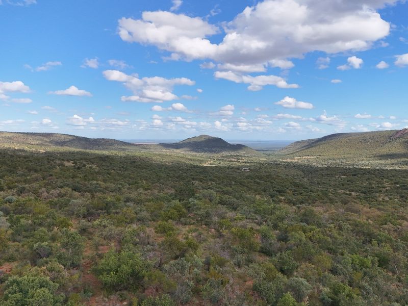 An expansive aerial view of the natural landscape, showcasing rolling hills and native vegetation under a clear blue sky.