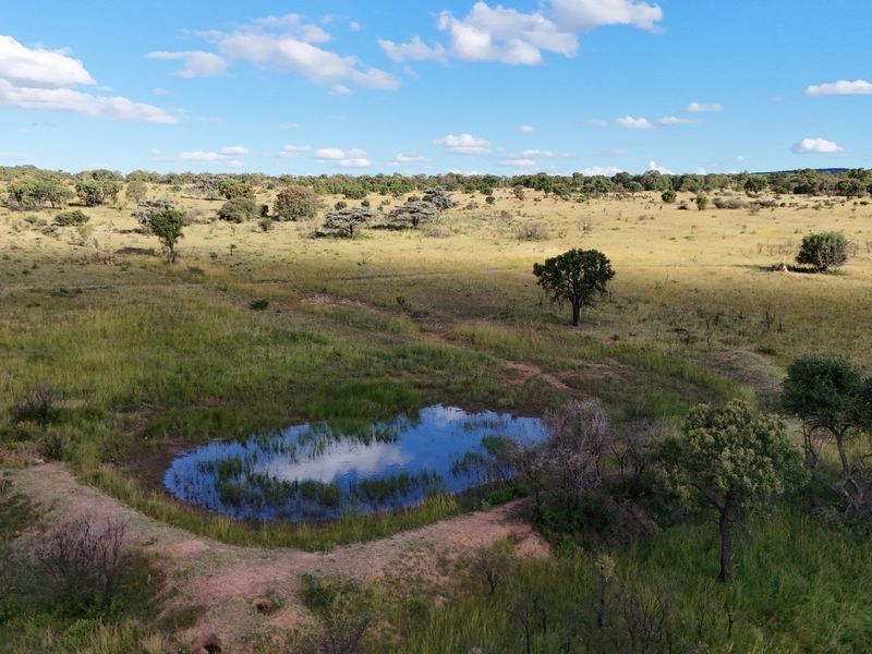 An aerial view of a vast, open residential land plot featuring natural grassland and a small water feature.