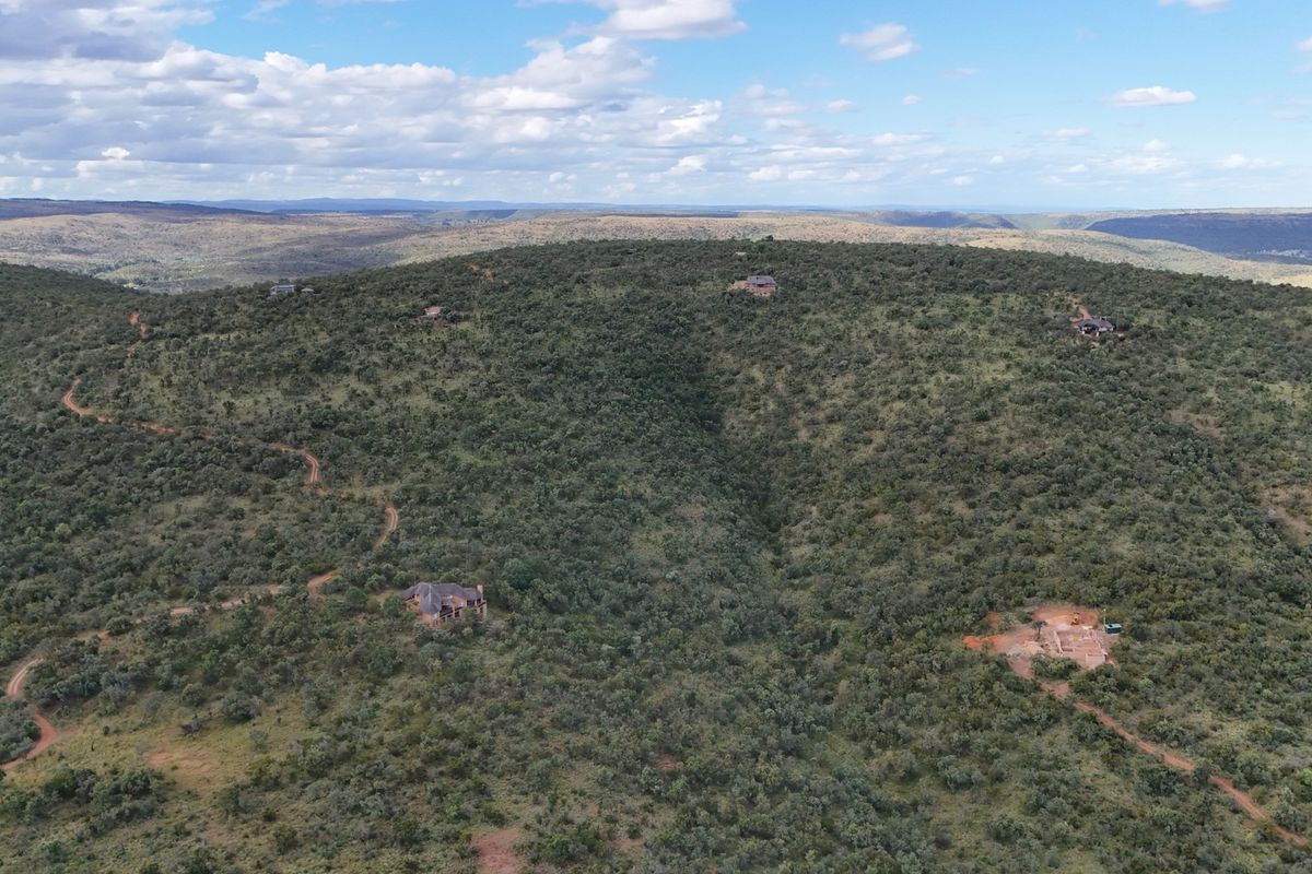 An aerial view of a vast, hilly residential estate landscape featuring natural vegetation, dirt access roads, and scattered residential building sites.
