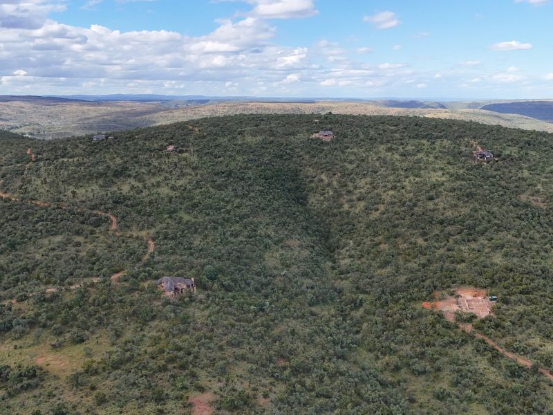 An aerial view of a vast, hilly residential estate landscape featuring natural vegetation, dirt access roads, and scattered residential building sites.