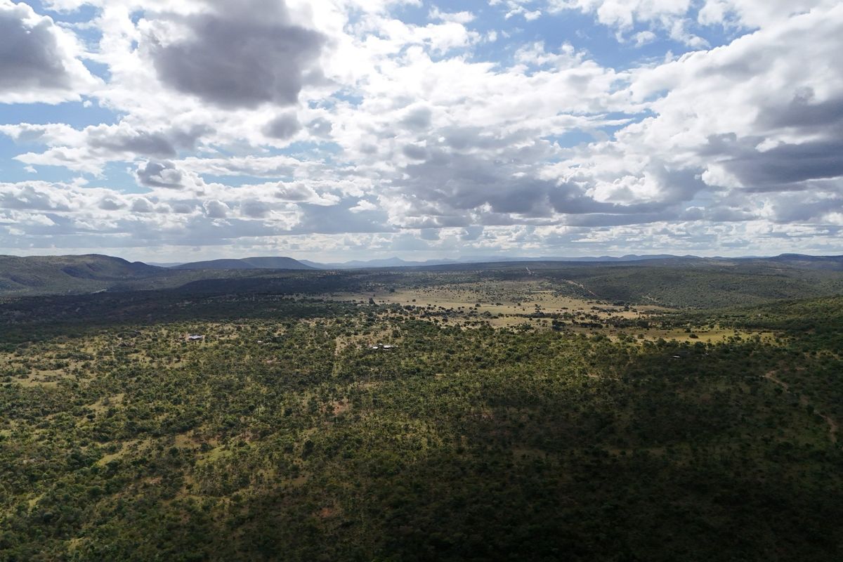 An expansive aerial view of the natural bushveld landscape, showcasing the vast terrain and surrounding hills under a cloudy sky.