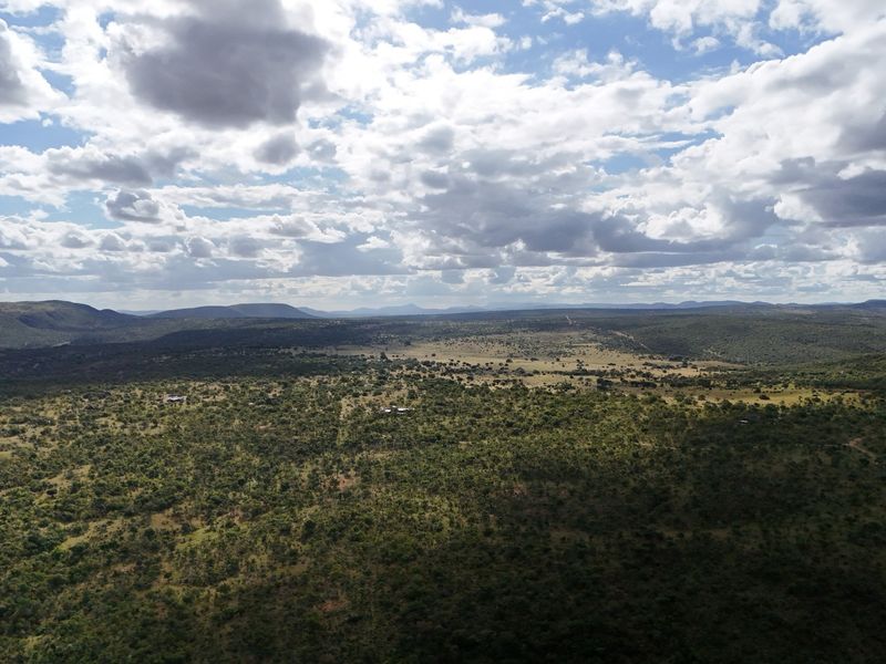 An expansive aerial view of the natural bushveld landscape, showcasing the vast terrain and surrounding hills under a cloudy sky.