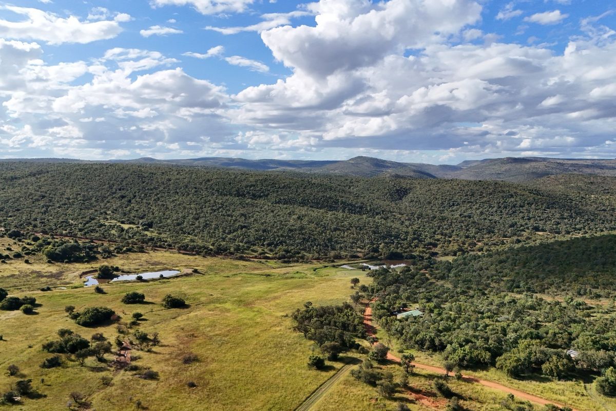 An aerial view of a vast, undeveloped residential land parcel featuring rolling hills, natural vegetation, dirt access roads, and small water dams.